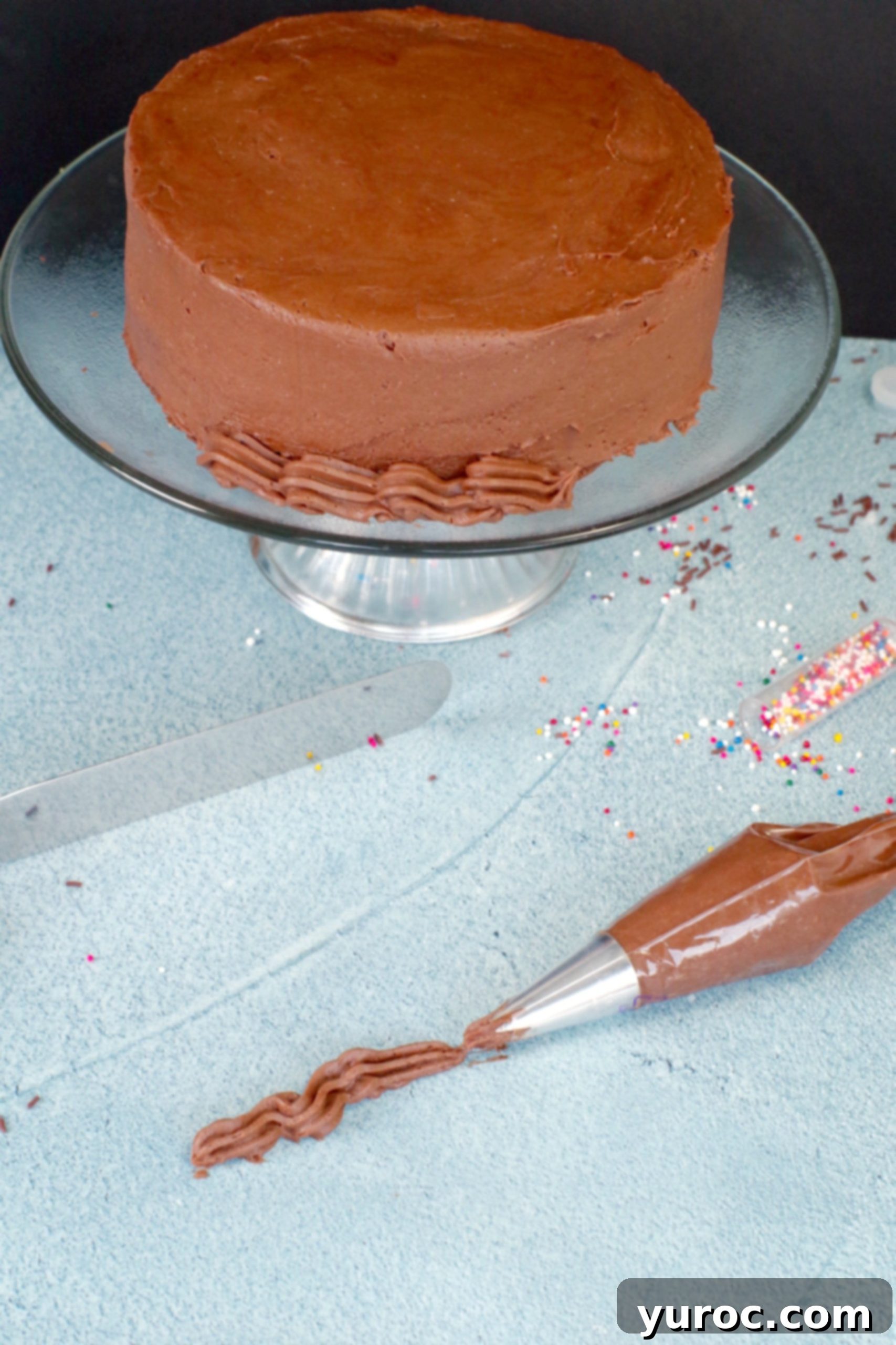 Chocolate frosting in a piping bag with a beautifully decorated cake in the background, showcasing the frosting's stability