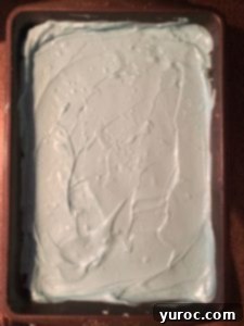 Pouring melted blue candy melts over Rice Krispie Treats in a 9x13 inch pan.