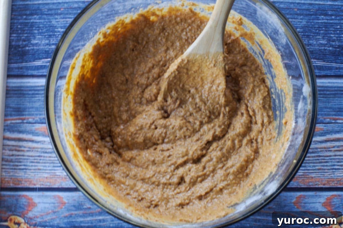 wet and dry ingredients mixed together in a large glass bowl with wooden spoon