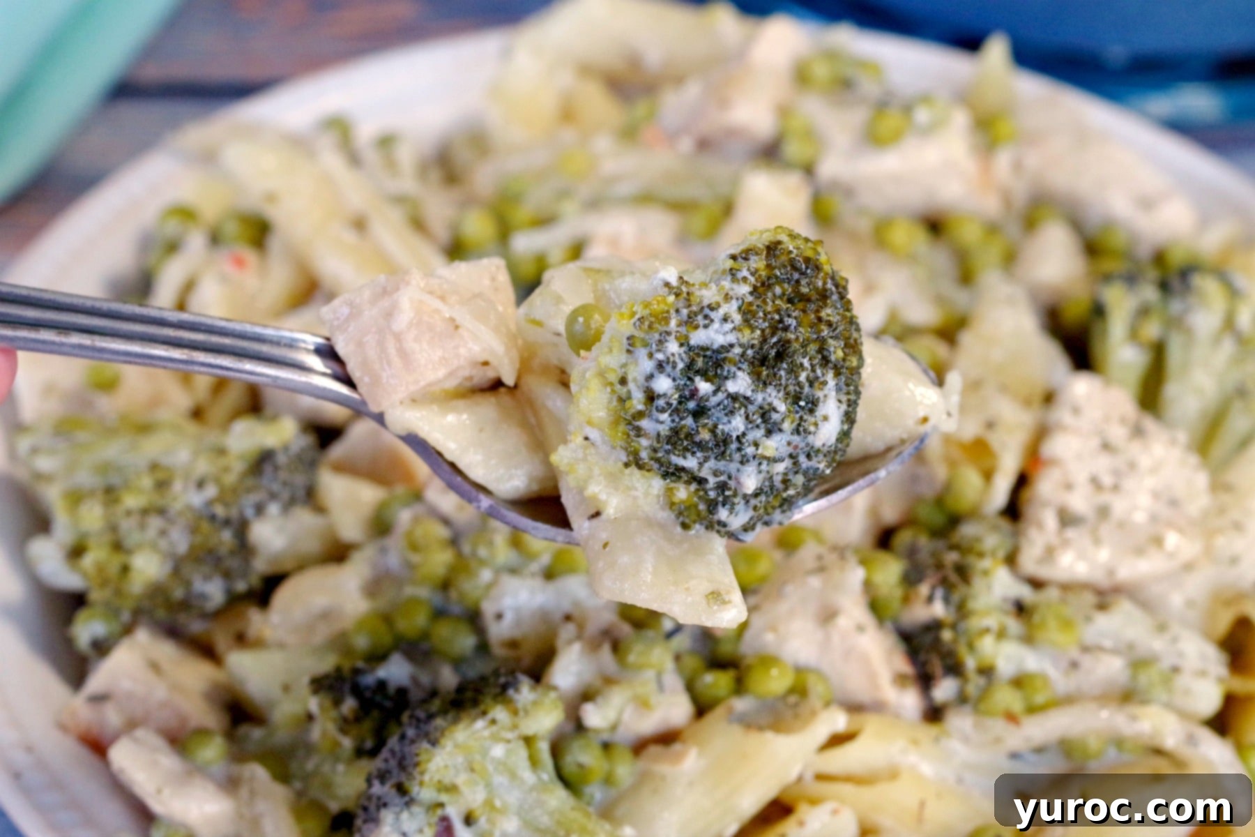 Cream Lemon Chicken pasta in a bowl with a spoonful being held up close to camera