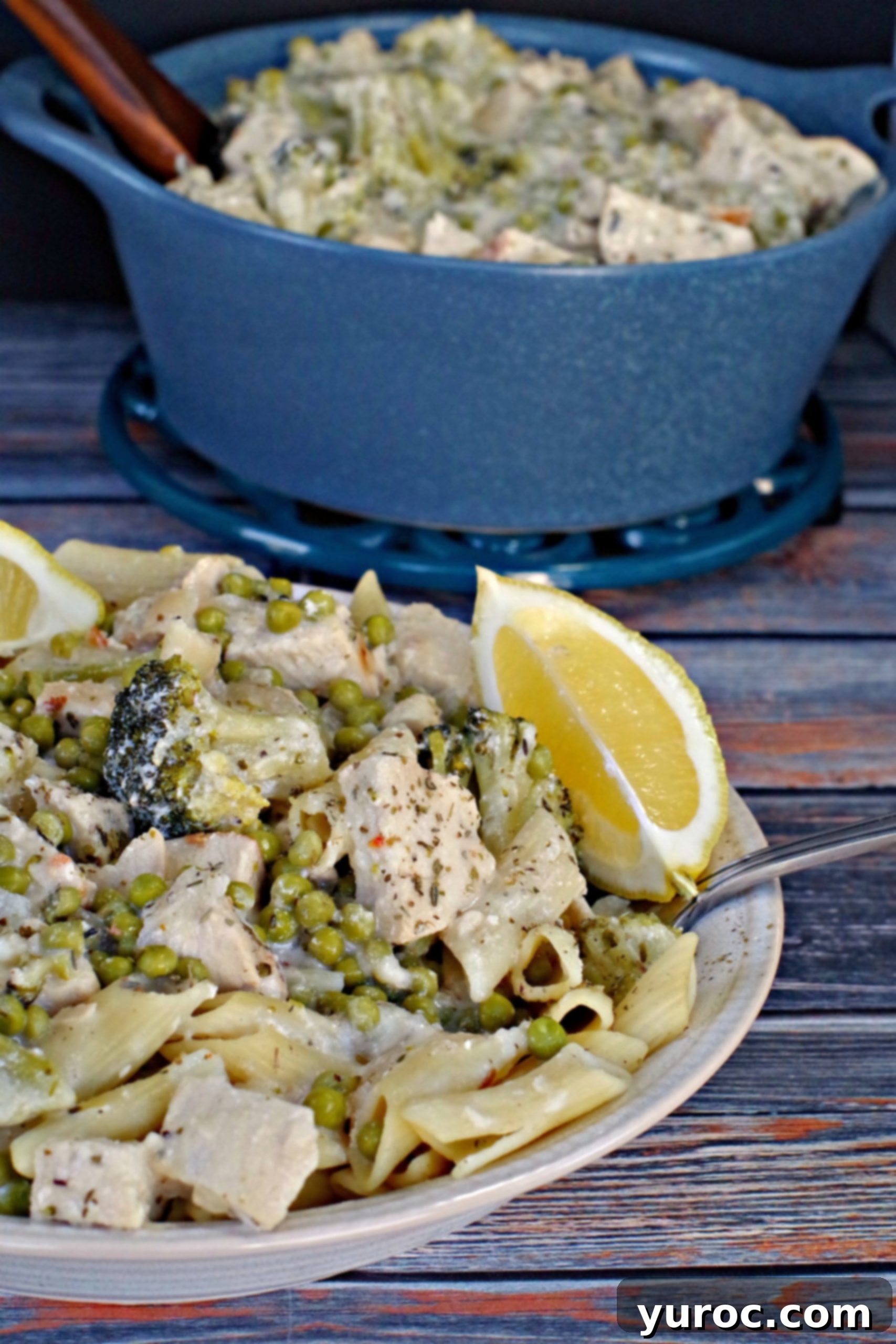 Creamy Lemon Chicken Pasta in a bowl with lemon wedges and blue ceramic pot in background