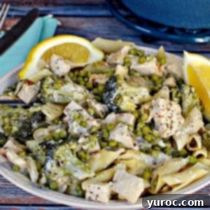 creamy lemon chicken pasta in a beige bowl with lemons on side, on blue surface