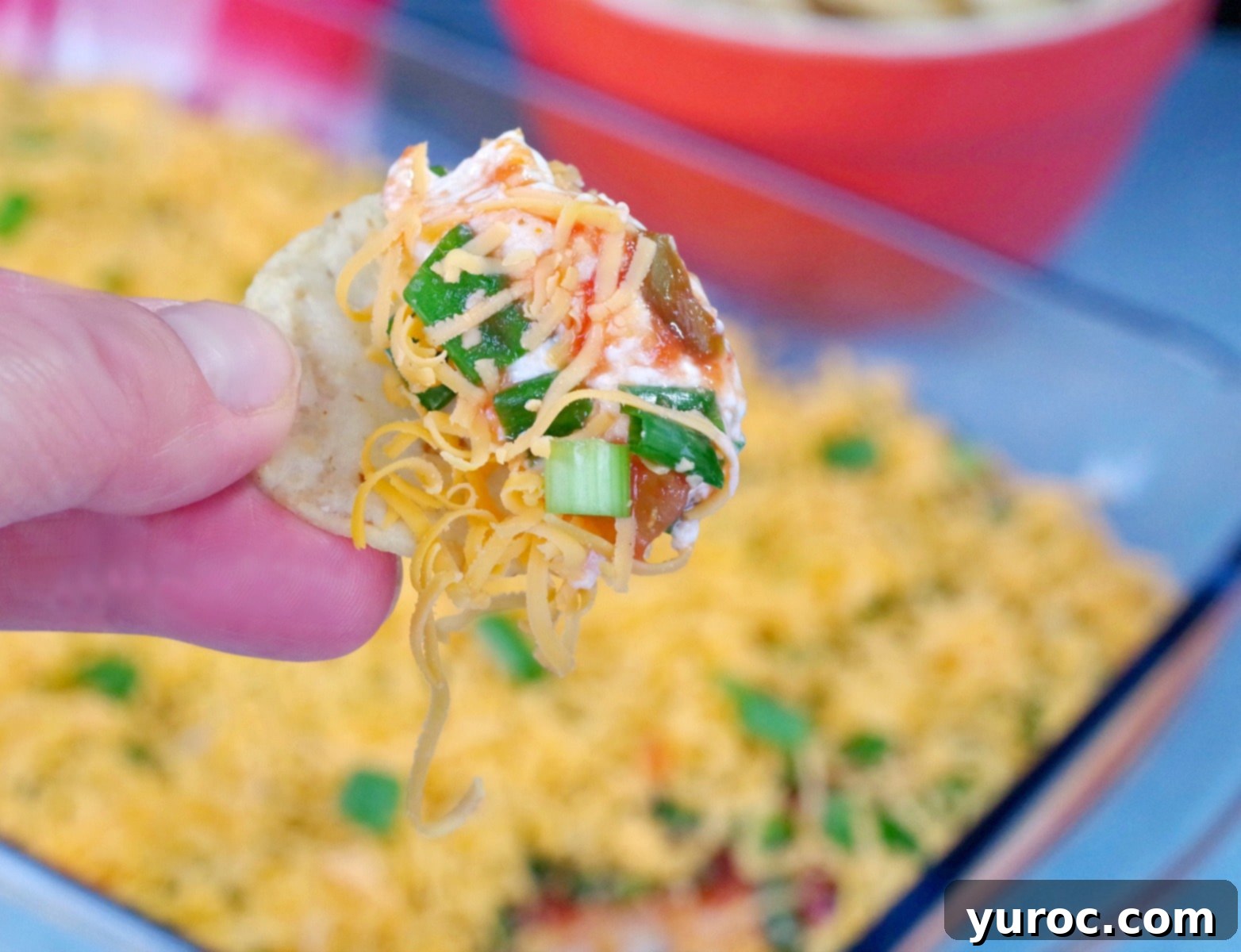 Effortless Stacked Nacho Delight 2 A nacho chip being dipped into a vibrant, cold layered nacho dip, showcasing its delicious layers.