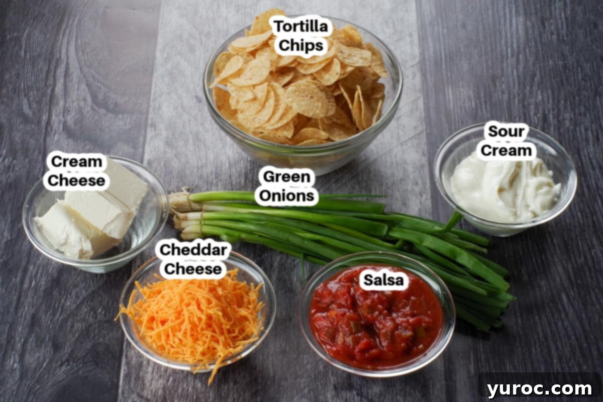 Effortless Stacked Nacho Delight 3 Individual bowls containing shredded cheese, salsa, sour cream, cream cheese, and chopped green onions, ready for assembling the nacho dip.