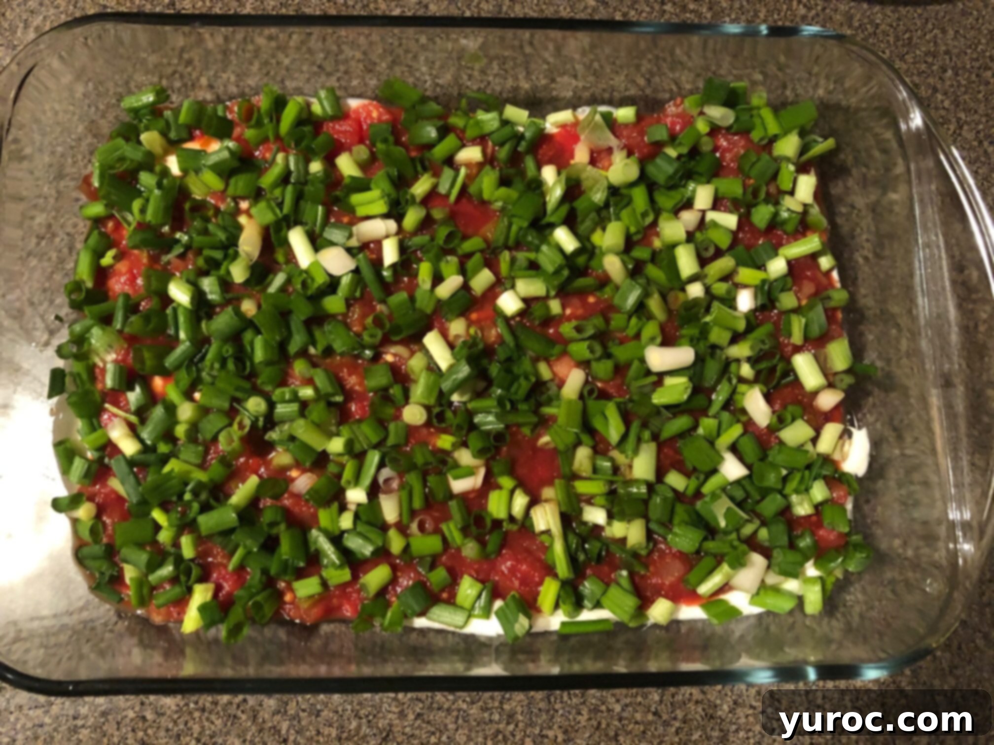 Effortless Stacked Nacho Delight 5 Chopped green onions sprinkled generously over a layer of salsa in a glass dish, creating a fresh and colorful third layer for the nacho dip.