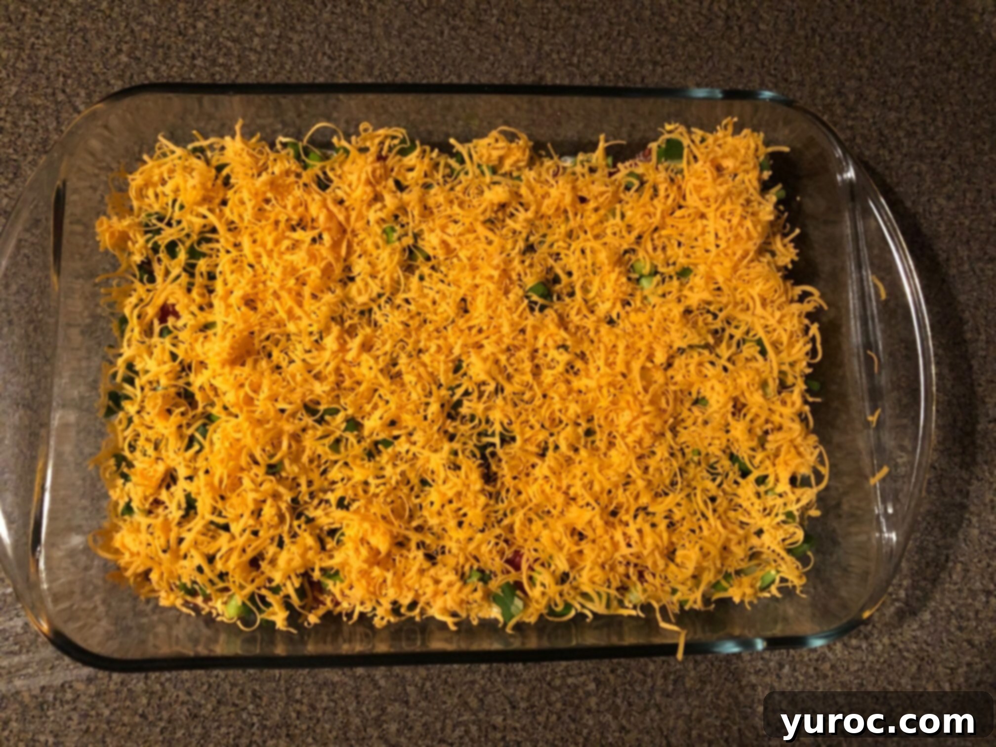 Effortless Stacked Nacho Delight 6 A finished layered nacho dip in a glass dish, topped with finely grated cheese and a sprinkle of green onions, ready for serving with tortilla chips.