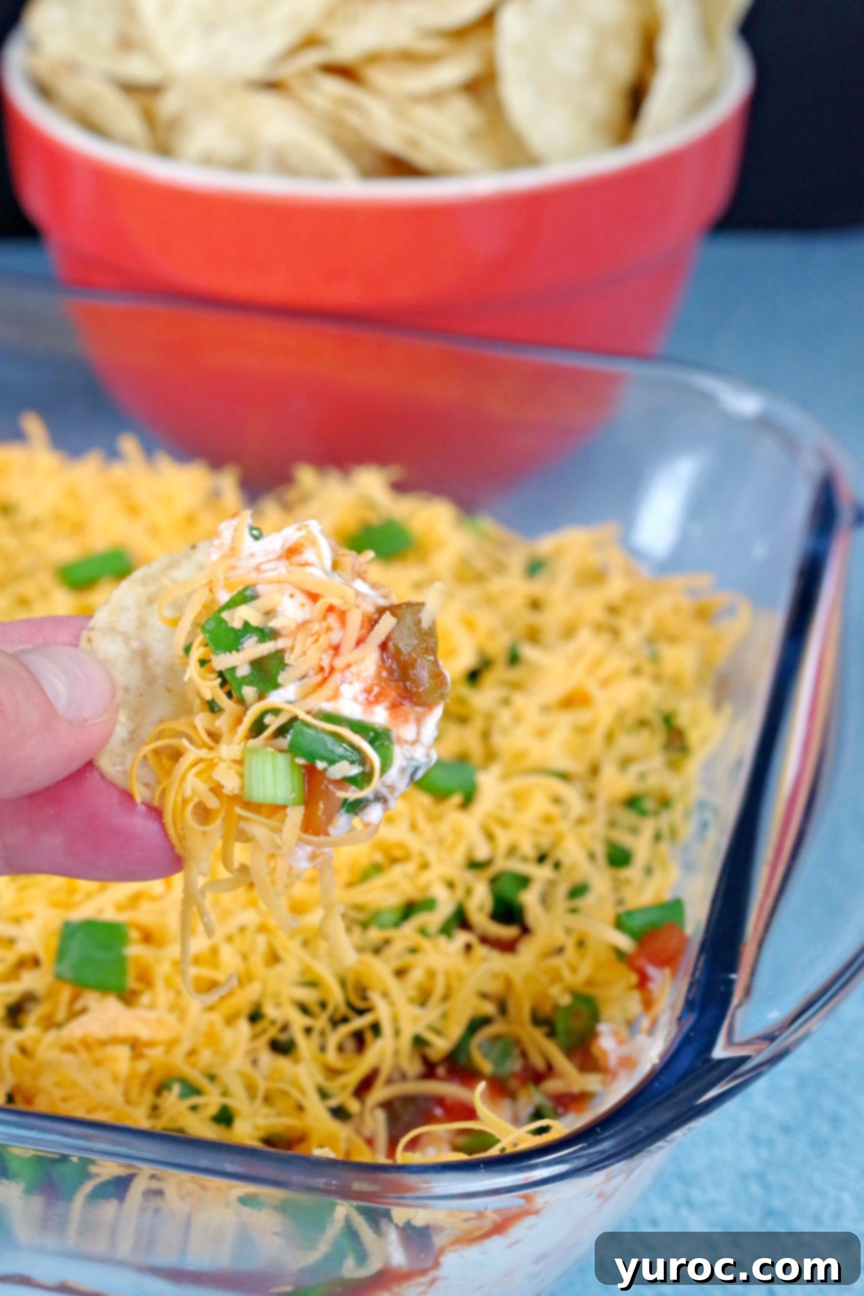 Effortless Stacked Nacho Delight 9 A tortilla chip being perfectly dipped into the creamy and flavorful layered nacho dip, highlighting its scoopability and delicious texture.
