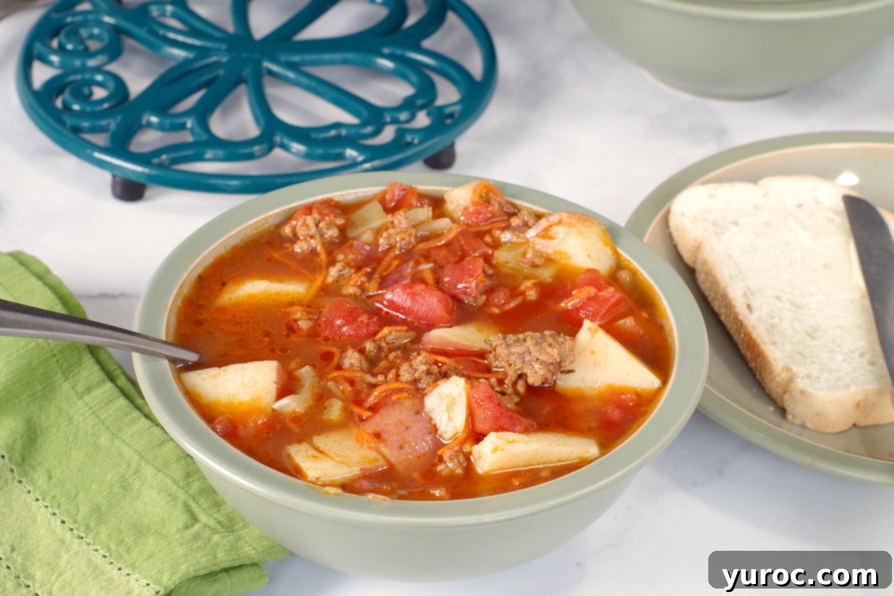 Hamburger soup in a green bowl with pot holder in background
