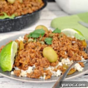 healthy picadillo over rice, on a plate with a fork and pan of more picadillo in the background