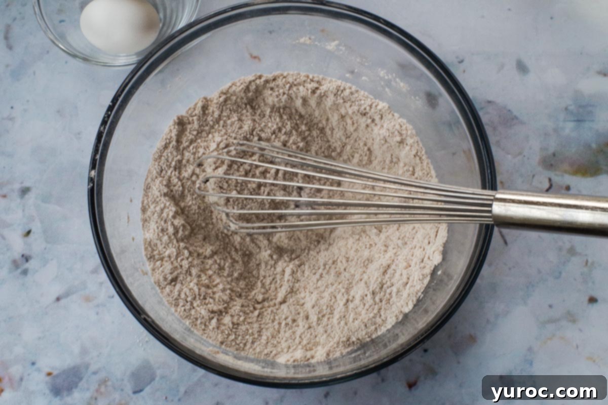Dry ingredients, including flour, sugar, baking powder, baking soda, and cinnamon, perfectly mixed together in a large glass bowl with a whisk.