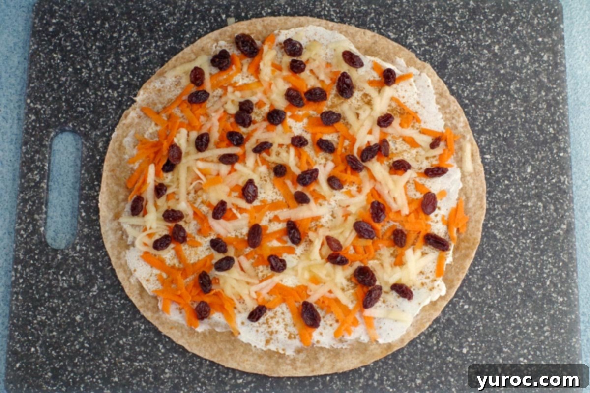 Cinnamon Raisin Tortilla Pinwheels 5 tortilla with cream cheese, cinnamon, shredded apple, shredded carrot and raisins on a cutting board