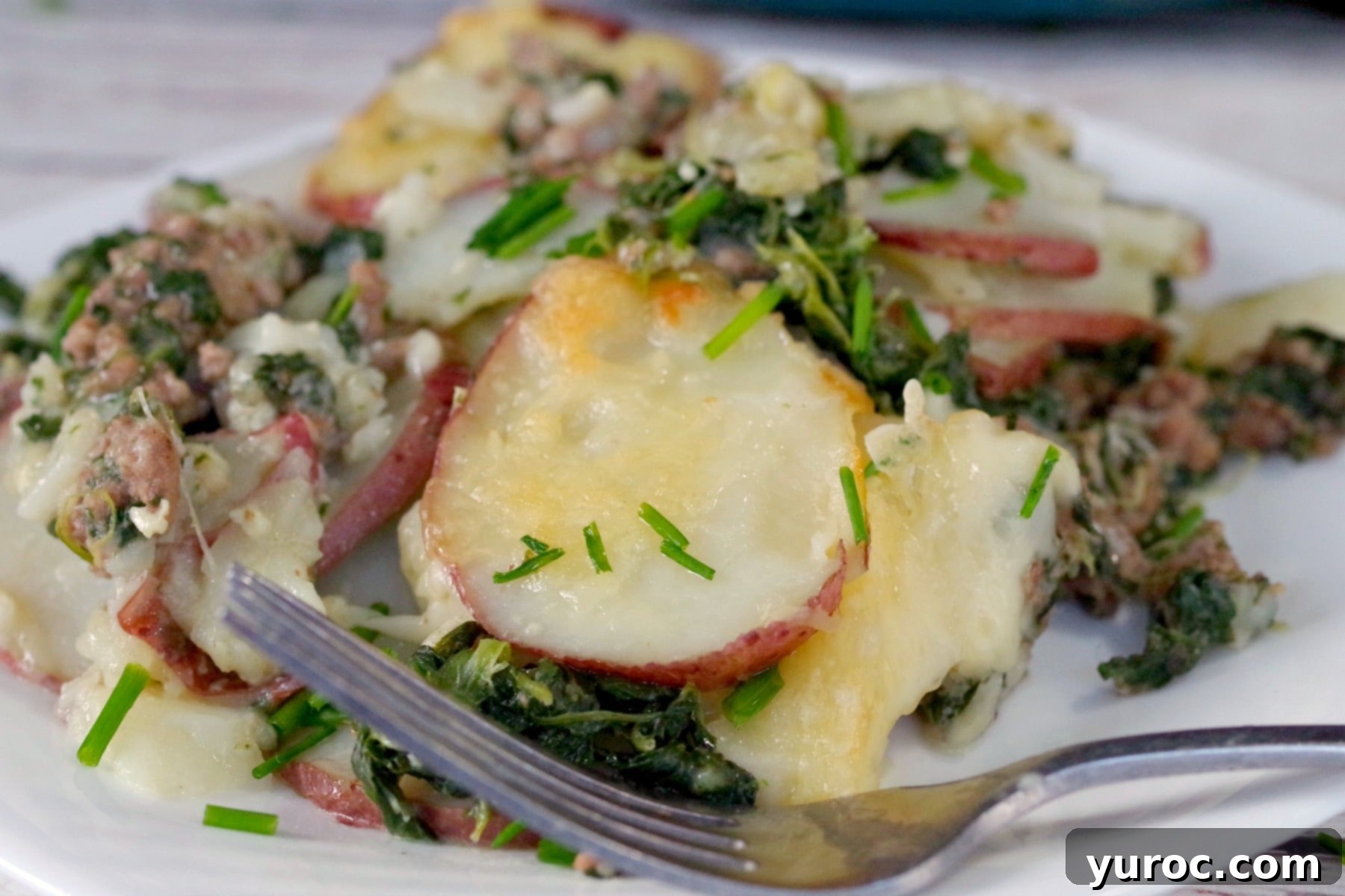 Close-up view of a perfectly portioned serving of Potato and Ground Beef Casserole with Spinach on a white plate, highlighting the delicious layers of potato, meat, and cheese.