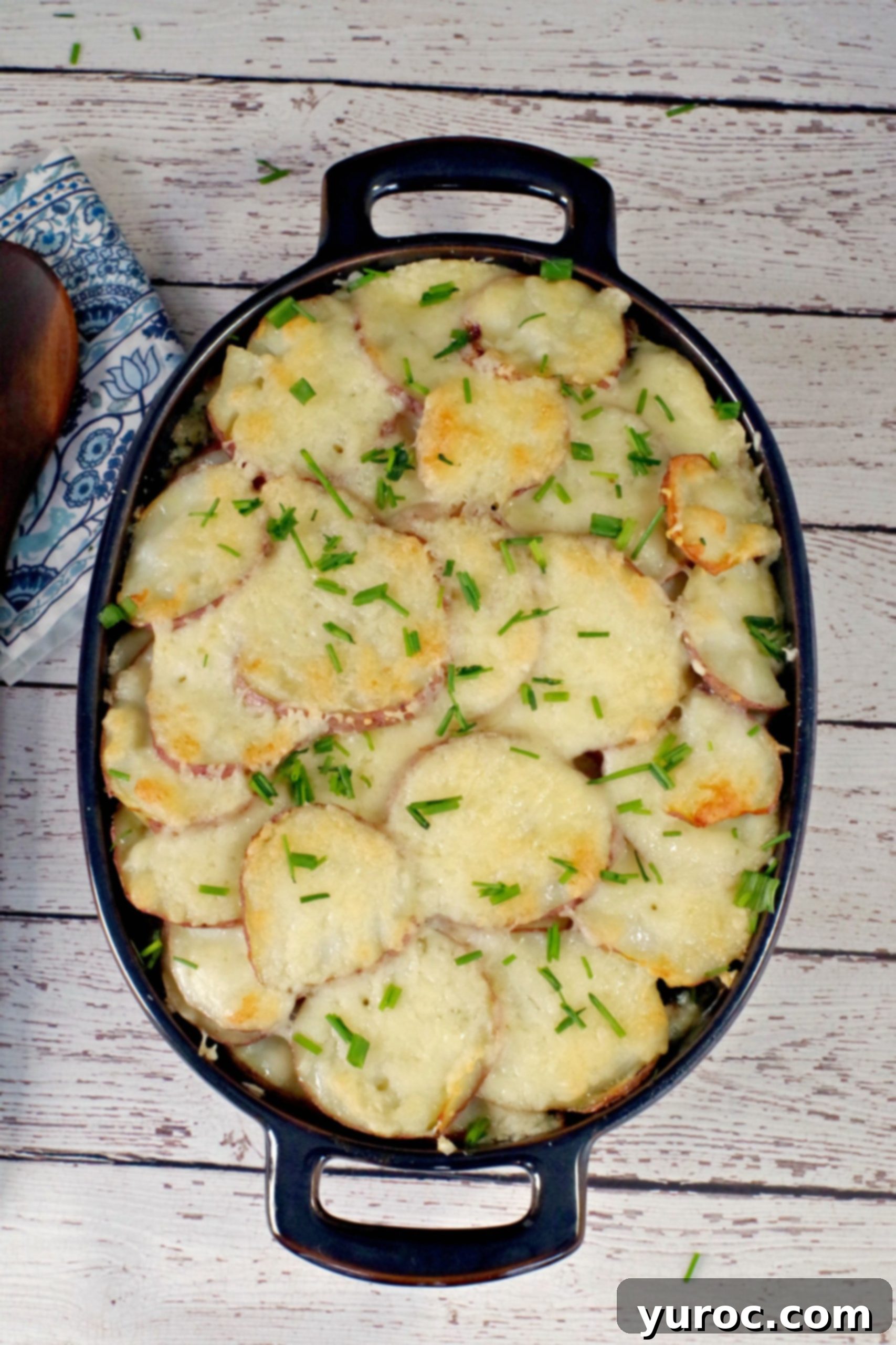 A large blue casserole dish filled with baked Potato and Ground Beef Casserole, topped with melted Swiss cheese and fresh chives, capturing its comforting and wholesome appeal.