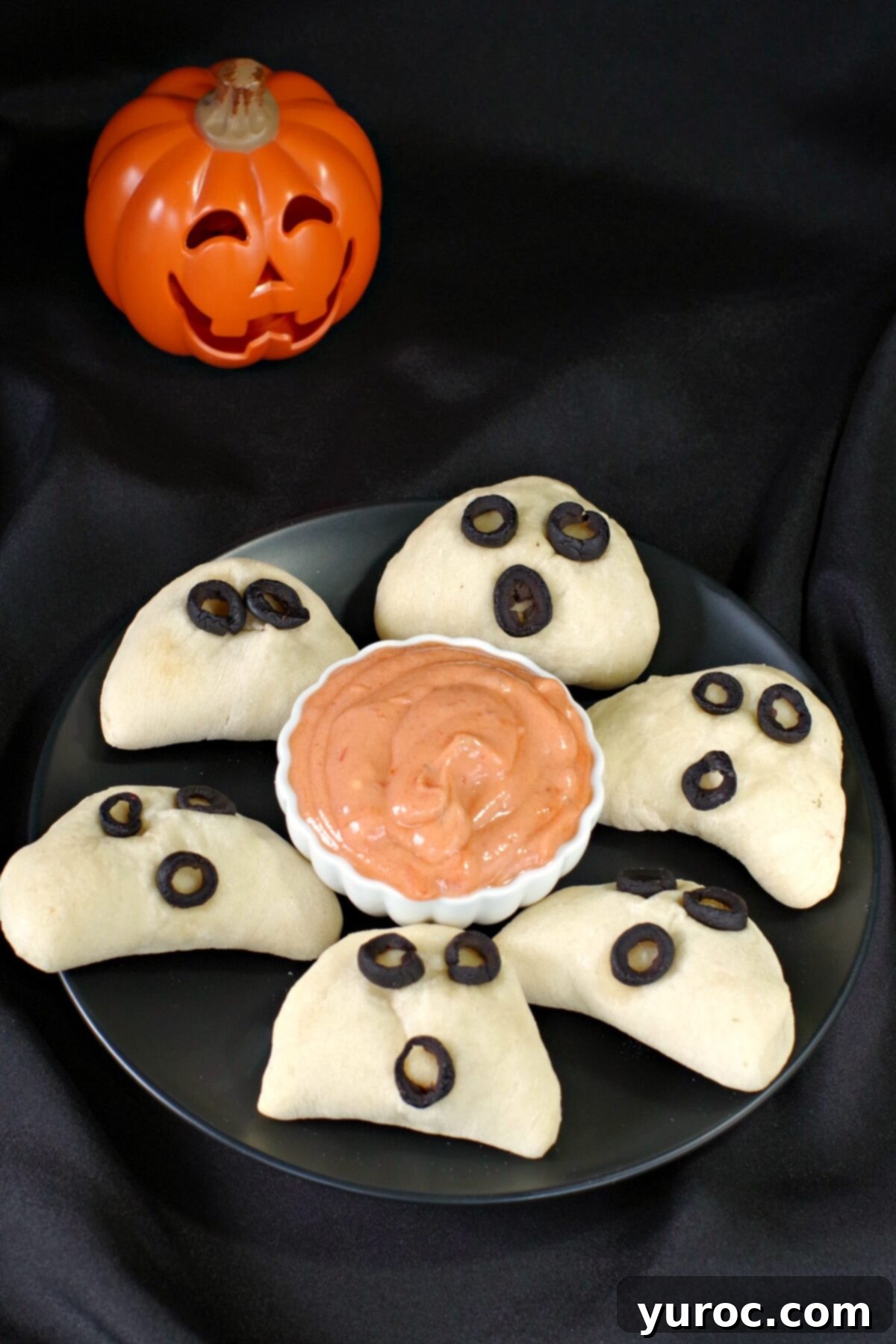 halloween pizza pockets on a black plate with dip in the middle and plastic jack o'latern in the background