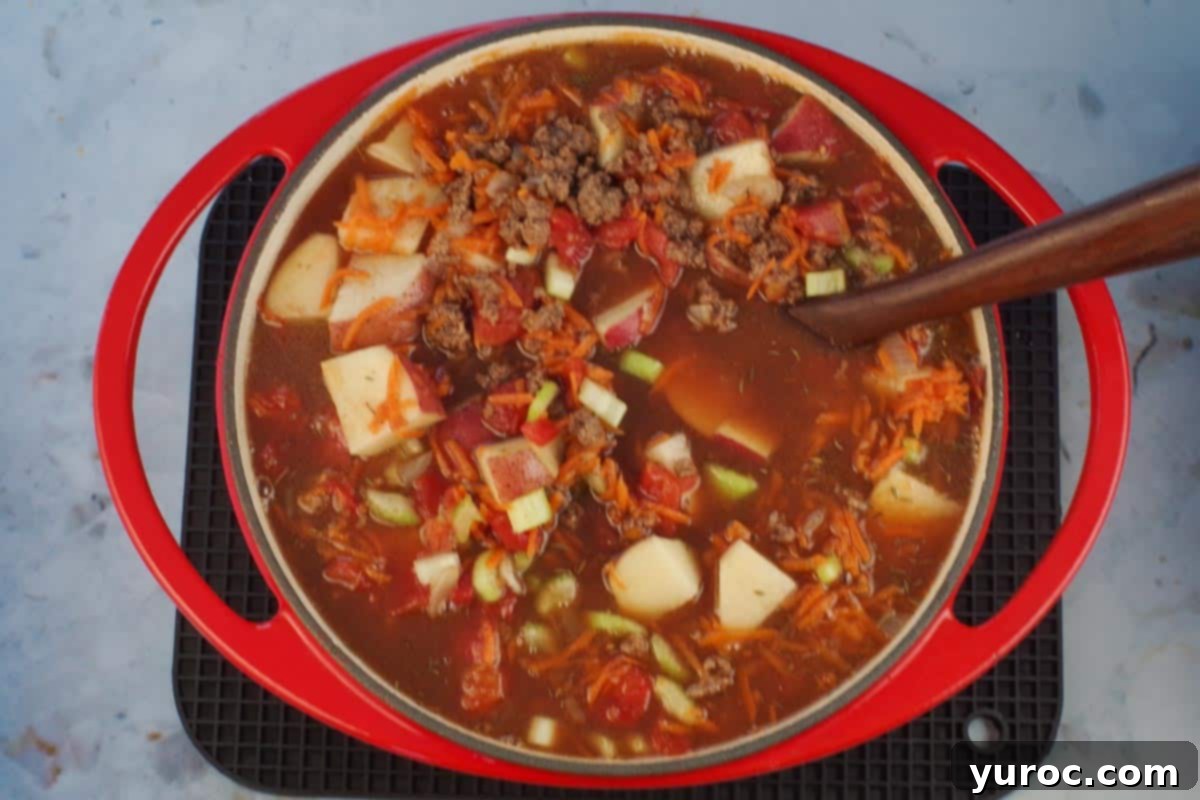Homestyle Hamburger Potato Soup 7 All ingredients for hamburger potato soup stirred together and simmering in the orange Dutch oven, creating a rich broth.