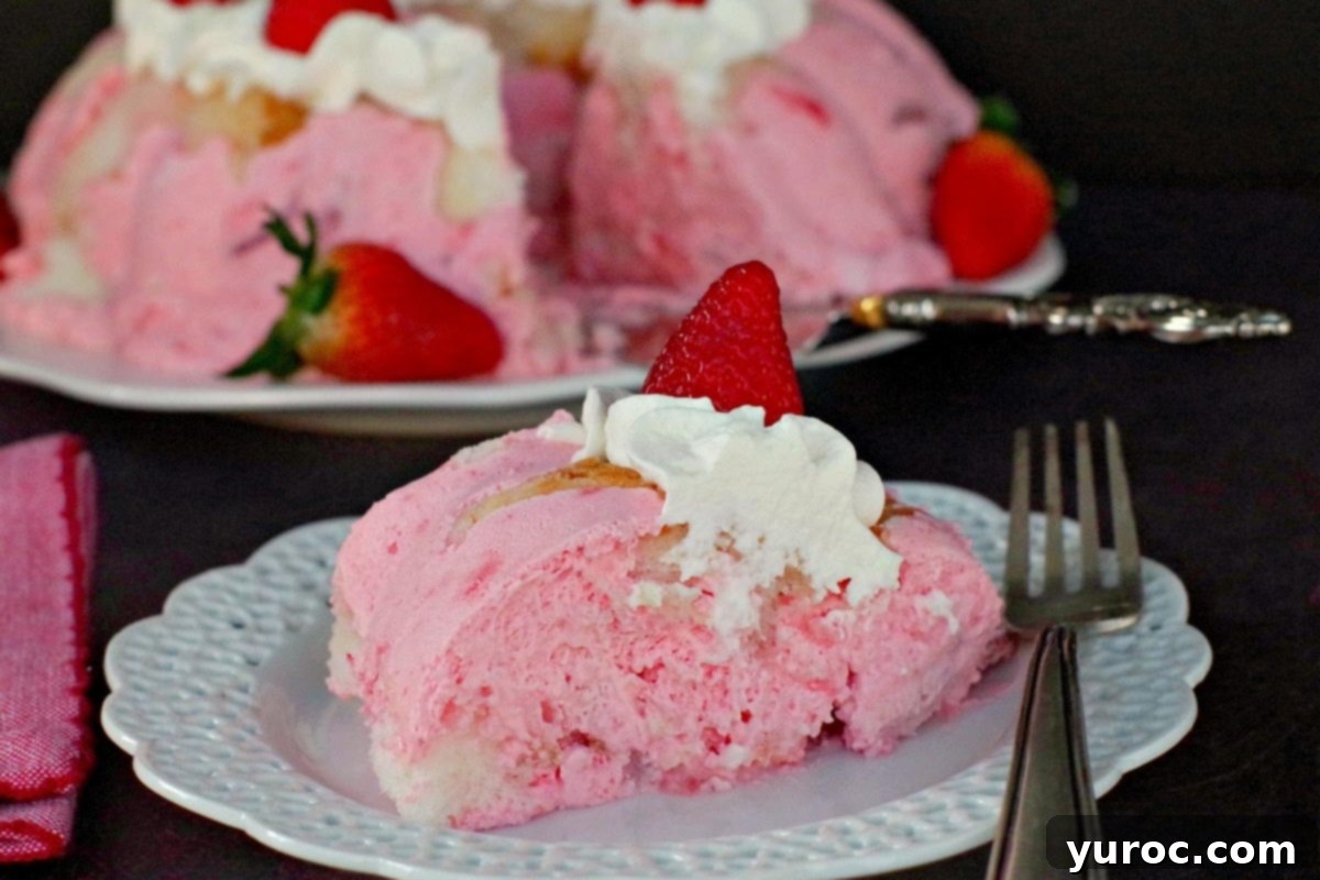 A slice of Strawberry Jello Angel Food cake on a white plate and a fork with the whole cake in the background. This no-bake dessert is perfect for spring and summer gatherings.