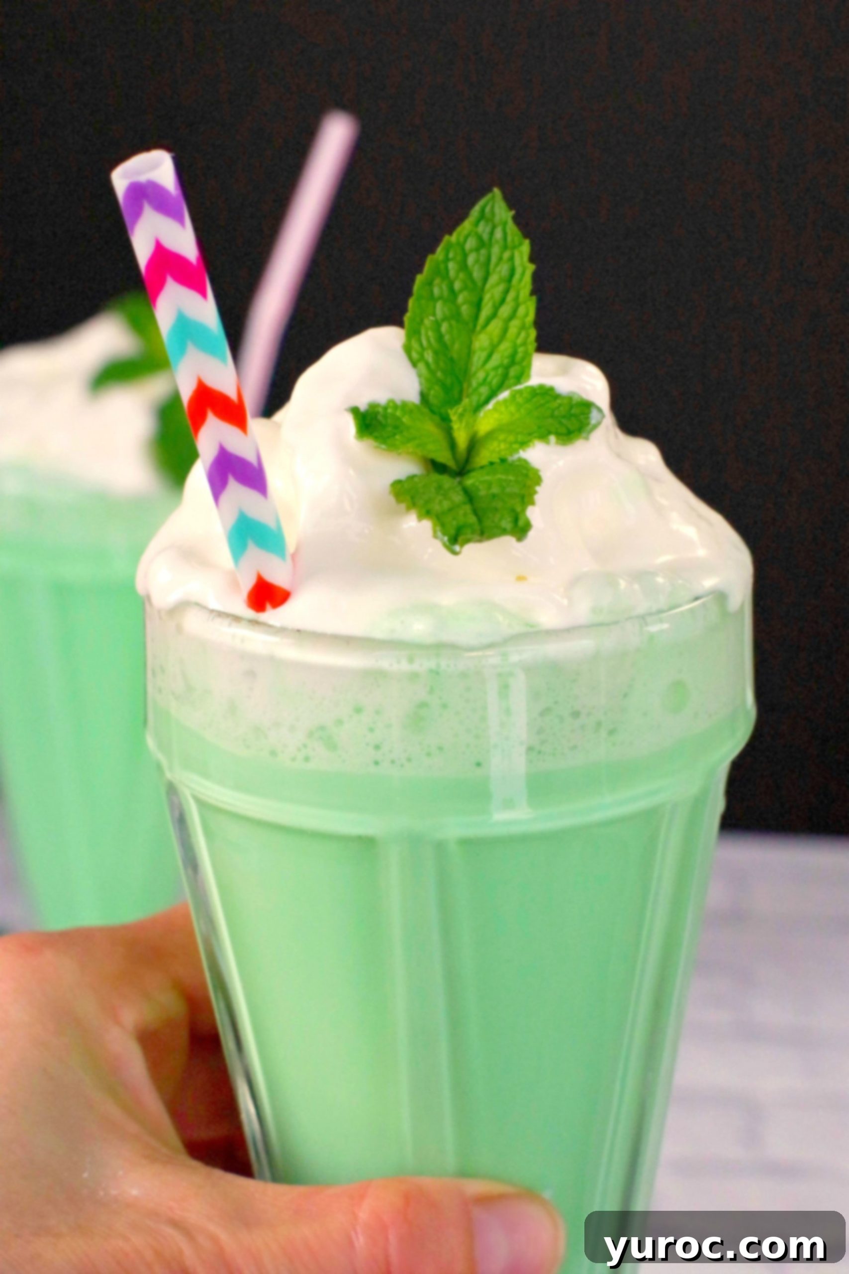 Emerald Grasshopper Mocktail 11 Two Green Grasshopper Mocktails, with a hand holding one in the foreground, showcasing its vibrant color.