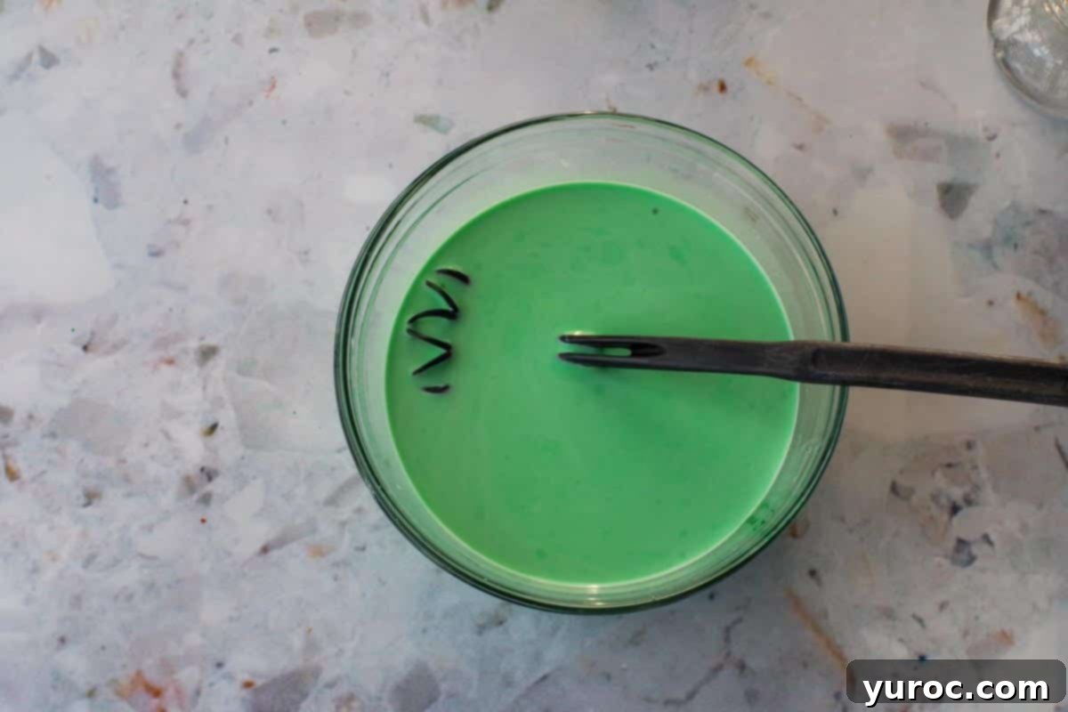 Emerald Grasshopper Mocktail 6 Green food coloring being added to the hot chocolate mixture in a bowl.