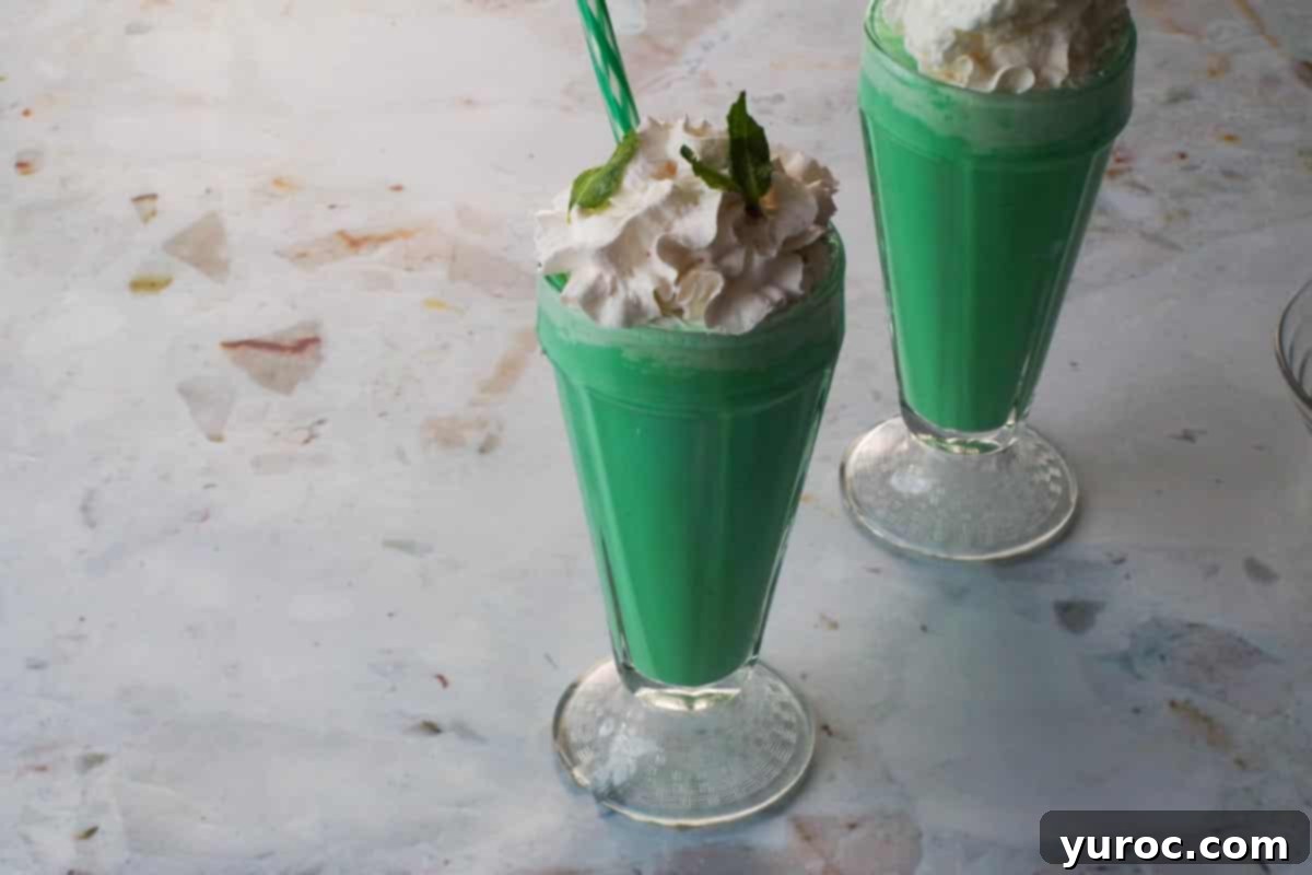 Emerald Grasshopper Mocktail 9 A finished Green Grasshopper Mocktail with whipped cream and fresh mint leaves garnish, complete with a green straw.