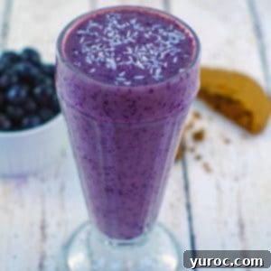 blueberry smoothie with almond milk on a white faux wooden surface with a half a cookie and blueberries in background