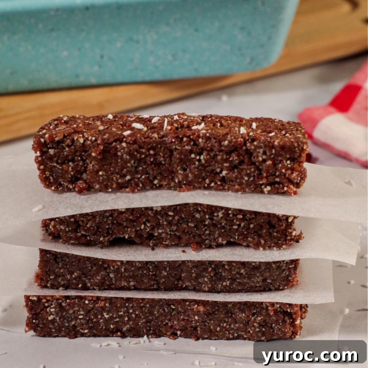 4 No bake energy bars stacked with parchment paper between them and blue loaf pan on cutting board in background