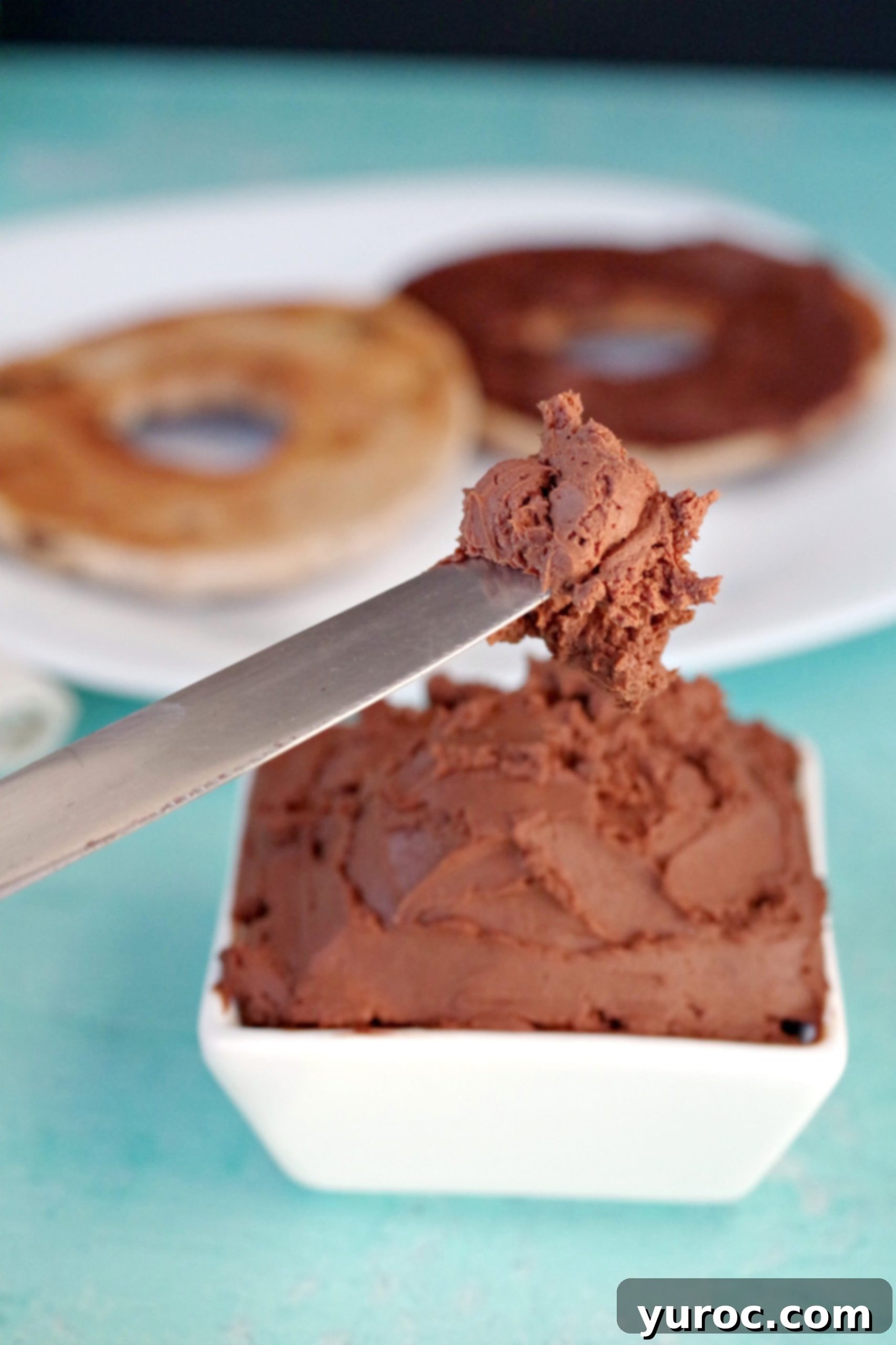 Decadent 3-Ingredient Chocolate Cream Cheese Spread 5 Close-up of a knife spreading rich homemade chocolate cream cheese on a surface, with a bowl of the spread in the background.