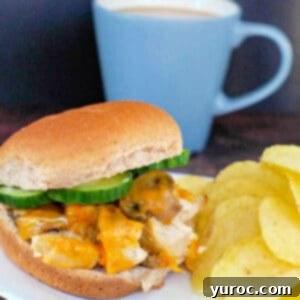 Chicken breast burger on a white plate with potato chips and a blue cup of coffee in the background.