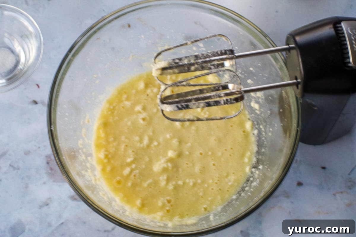 Adding beaten eggs to the creamed butter and sugar mixture in a glass bowl