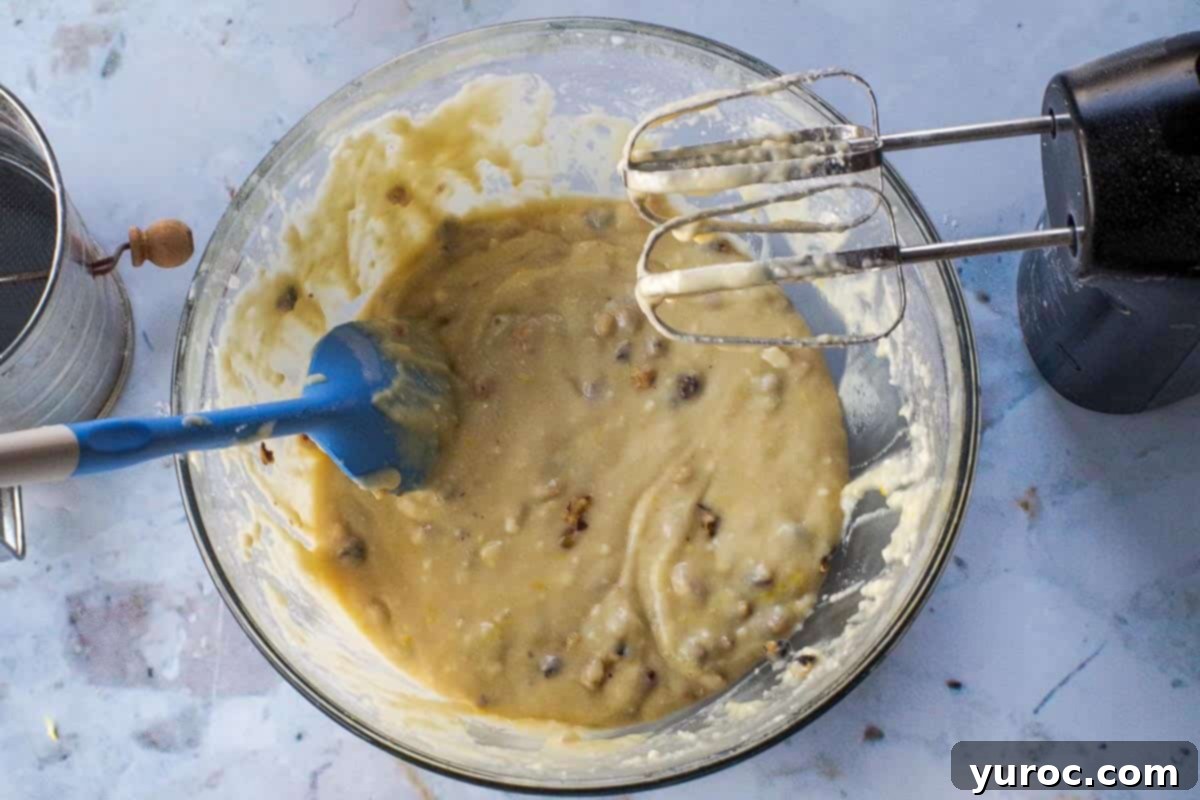 Chopped walnuts and lemon zest being stirred into the lemon bread batter in a glass bowl