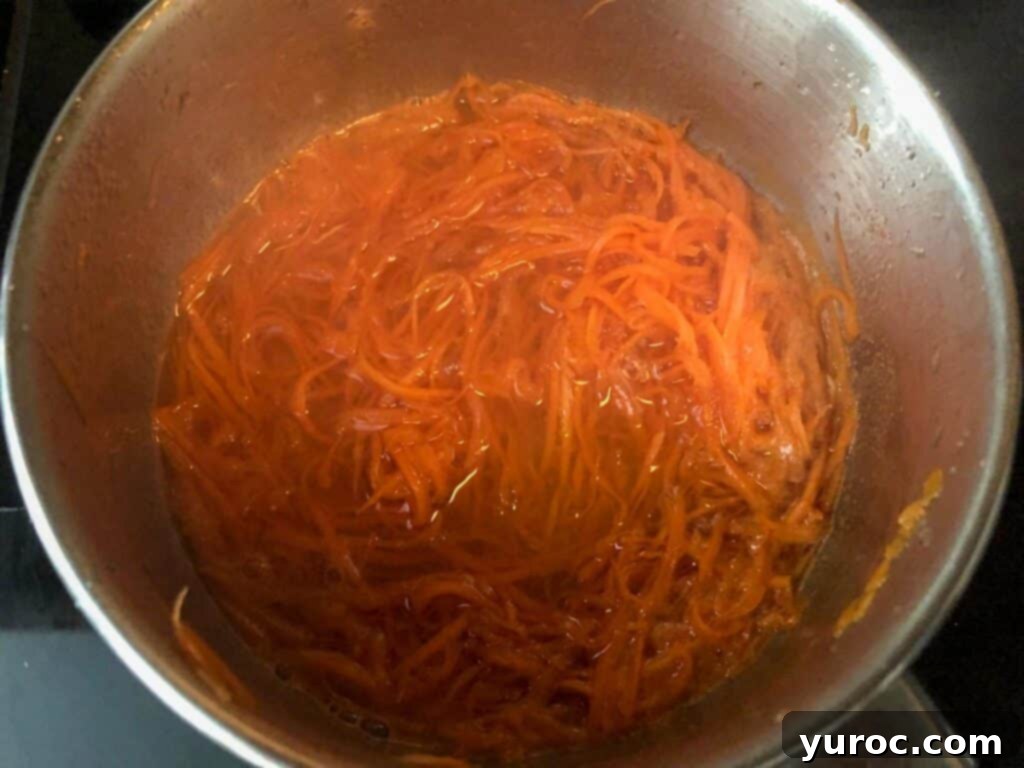 Shredded carrots cooking in a saucepan with sugar and water
