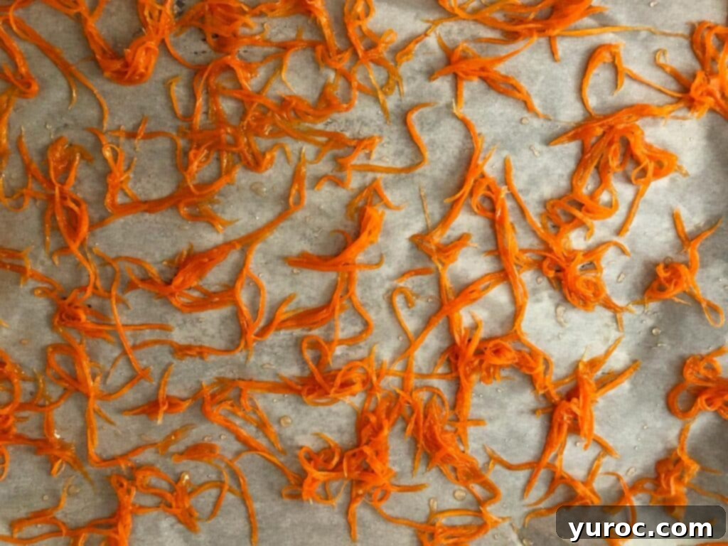 Drained candied carrot strips spread on a parchment-lined baking sheet
