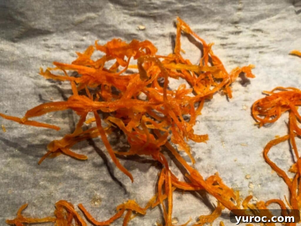 Dried candied carrot strips clumped together on parchment paper after drying