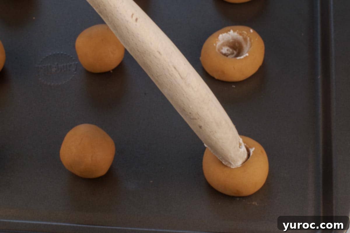 End of a wooden spoon dipped into powdered sugar making an indent in each cookie.