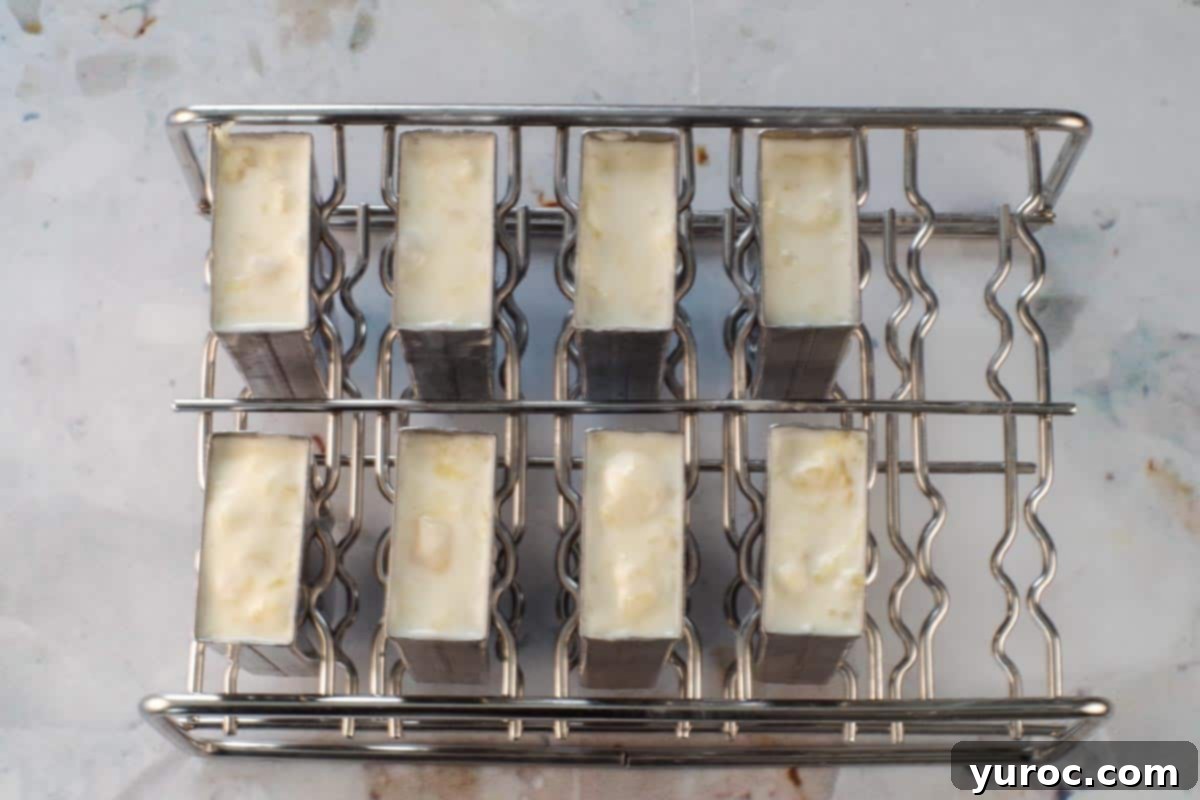 Cool & Creamy Virgin Pina Colada Pops 8 Piña Colada liquid mixture being carefully poured into individual popsicle molds.