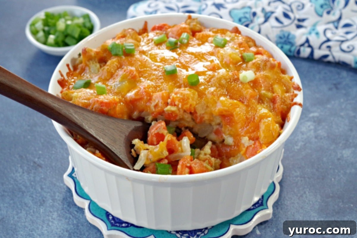carrot casserole in white casserole dish with a brown wooden spoon scooping casserole (on blue background) with dish of green onions and oven mitts in the background