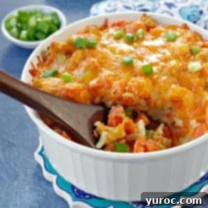 carrot casserole in white casserole dish with a brown wooden spoon scooping casserole (on blue background) with dish of green onions and oven mitts in the background