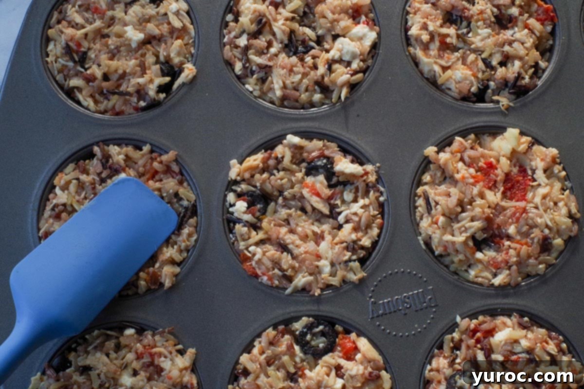 Zesty Mediterranean Chicken Rice Cups 8 Rice mixture being packed firmly into a muffin tin using a blue spatula
