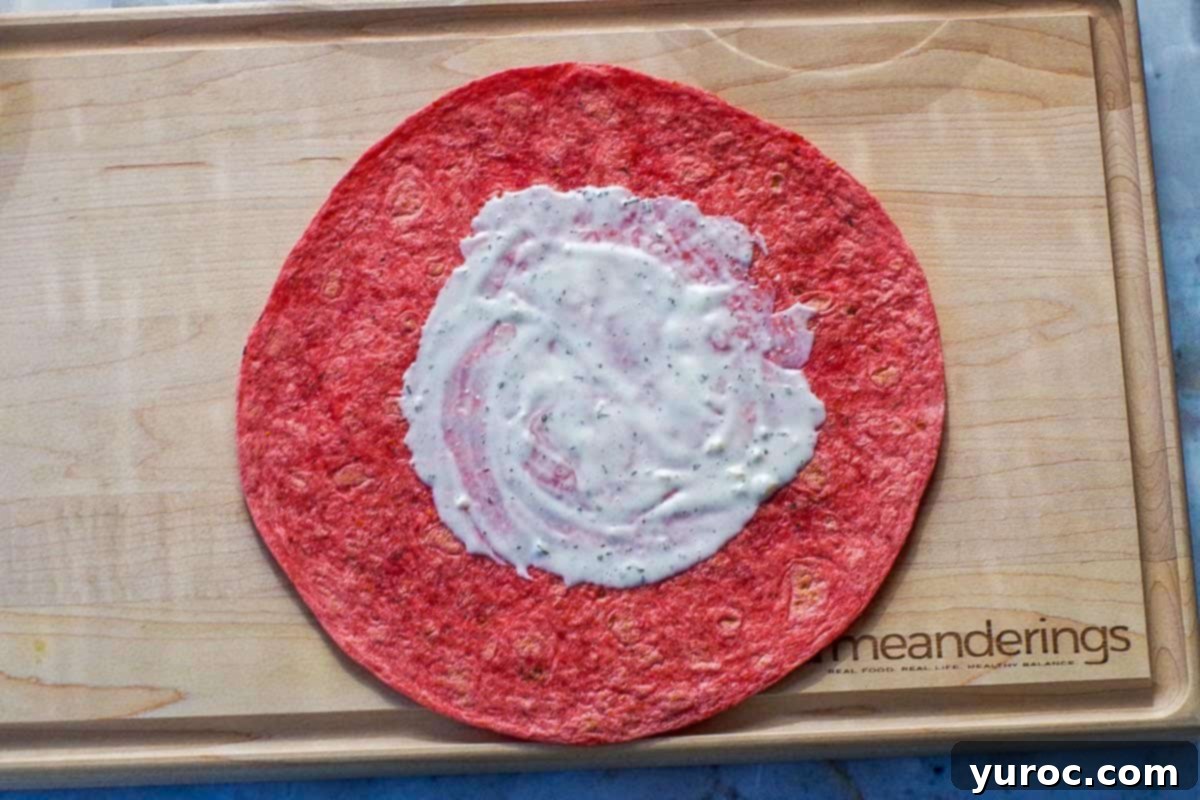 Ultimate Turkey Bacon Ranch Wrap 4 Tomato wrap with ranch dressing spread generously in the middle, forming the base layer.