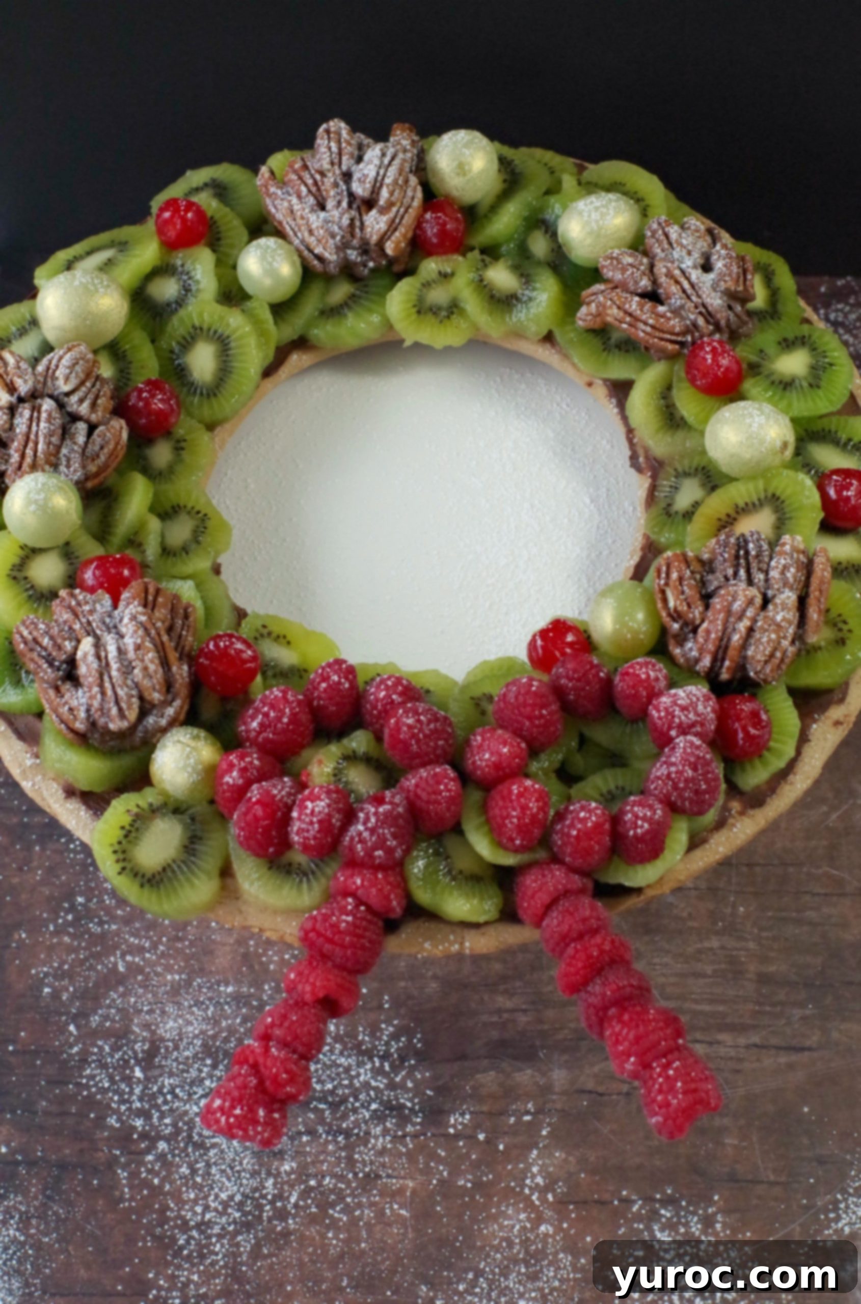 Gingerbread Edible Christmas Wreath with fruit and nuts, on brown wooden surface with powdered sugar sprinkles