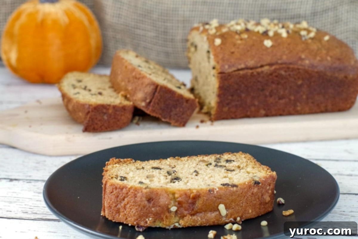 slice of pumpkin loaf on a black plate, with whole loaf on cutting board in background
