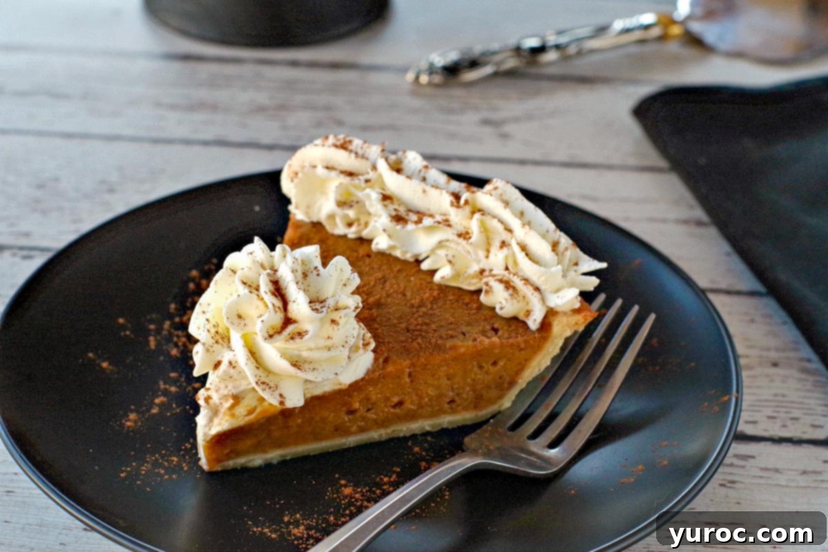 piece of pumpkin pie with whipped cream on a black plate with black platter stand in the background, with pie on platter
