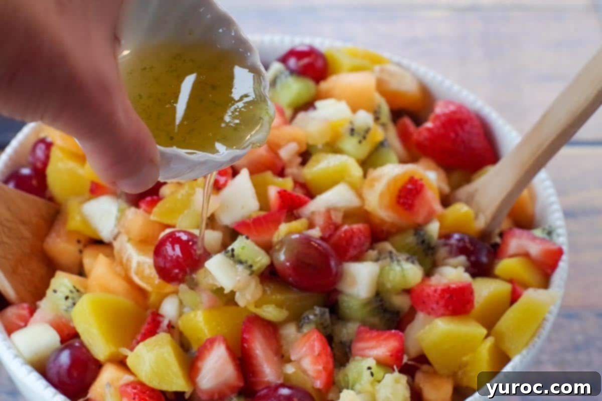 Stress-Free Christmas Breakfast Bake 7 easy fruit salad in white bowl with honey lime dressing being poured over salad
