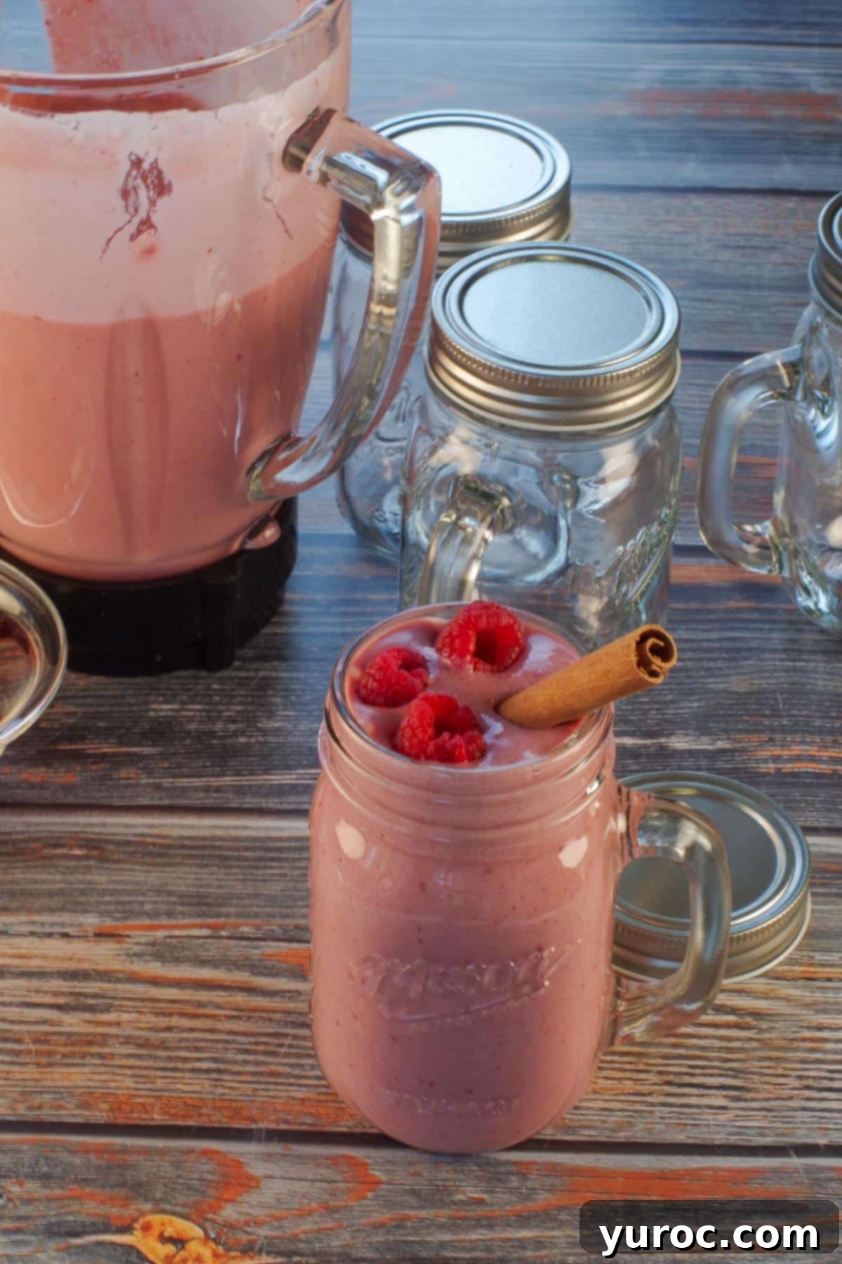 full glass of gingerbread smoothie garnished with raspberries and cinnamon stick with empty glasses and blender in the background