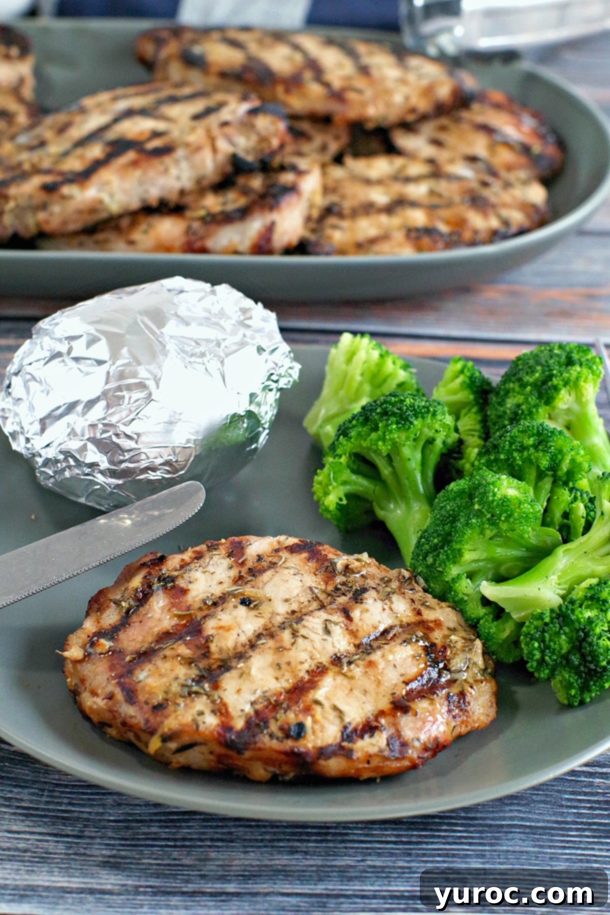 Maple lemon pork on a plate with broccoli and baked potato in foil with platter of pork in the backgroun