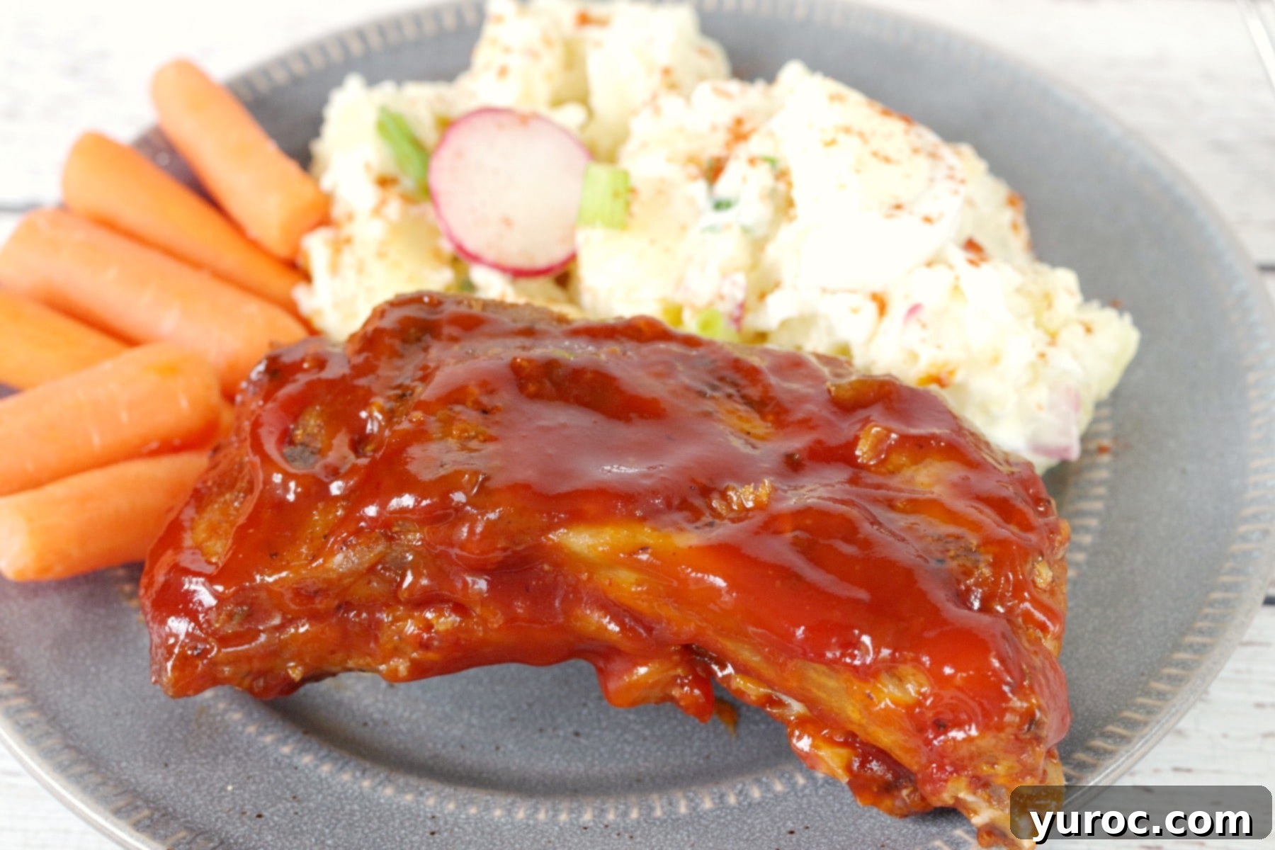 slow cooker BBQ beer ribs on a plate with potato salad and carrots