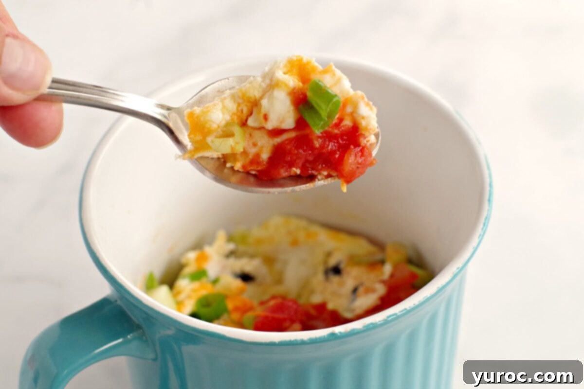 Delicious and fluffy Microwave Omelette in a Mug being held up on a spoon, ready to be enjoyed.