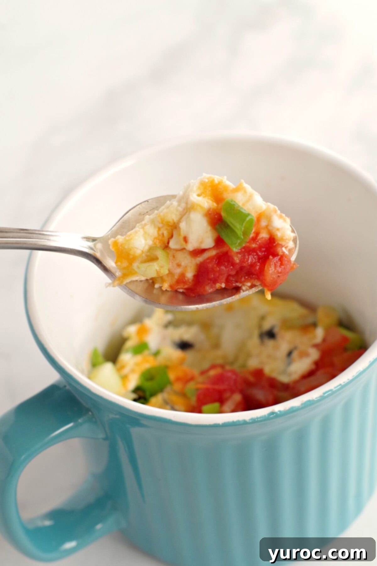 A fluffy, golden-brown microwave mug omelette held elegantly on a spoon, hovering over a vibrant blue mug, ready to be eaten as a healthy, quick breakfast.