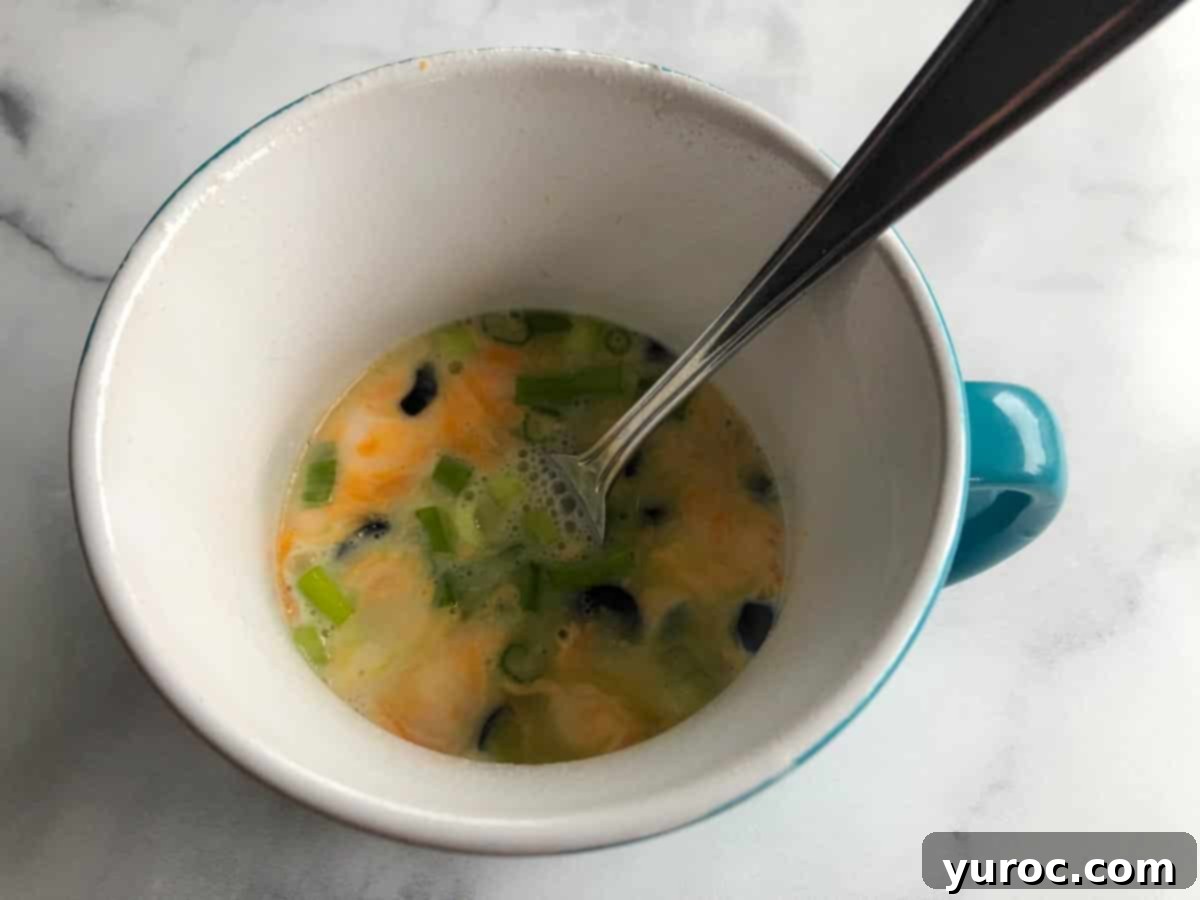 The omelette mixture being vigorously beaten with a fork inside the microwave-safe mug.