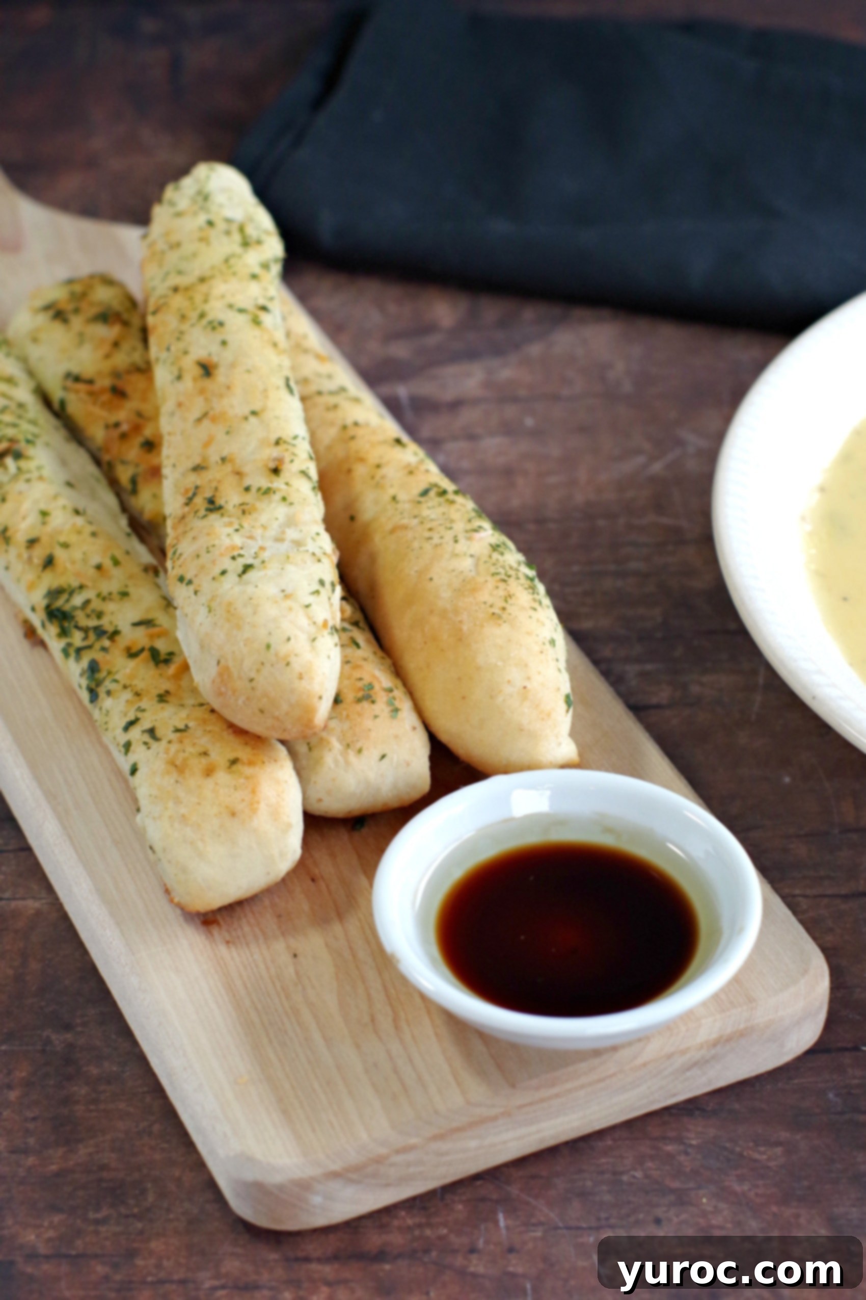 Freshly baked bread machine Italian breadsticks arranged on a wooden board, with a dipping bowl of balsamic vinegar and olive oil.