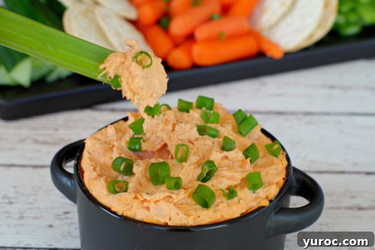 Crisp celery sticks being dipped into creamy buffalo chicken dip, highlighting a healthy serving option.